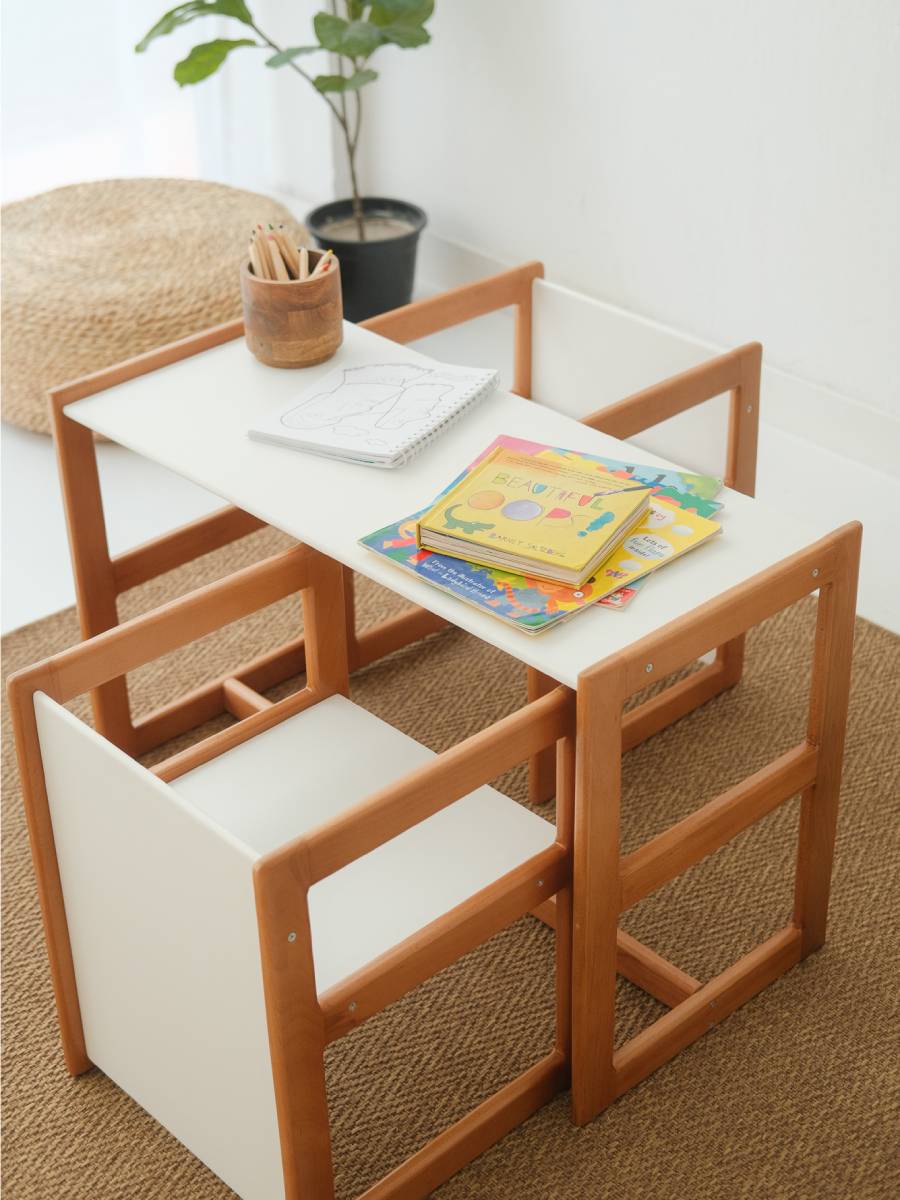 Children's wooden table and chairs set with a book on a white surface.